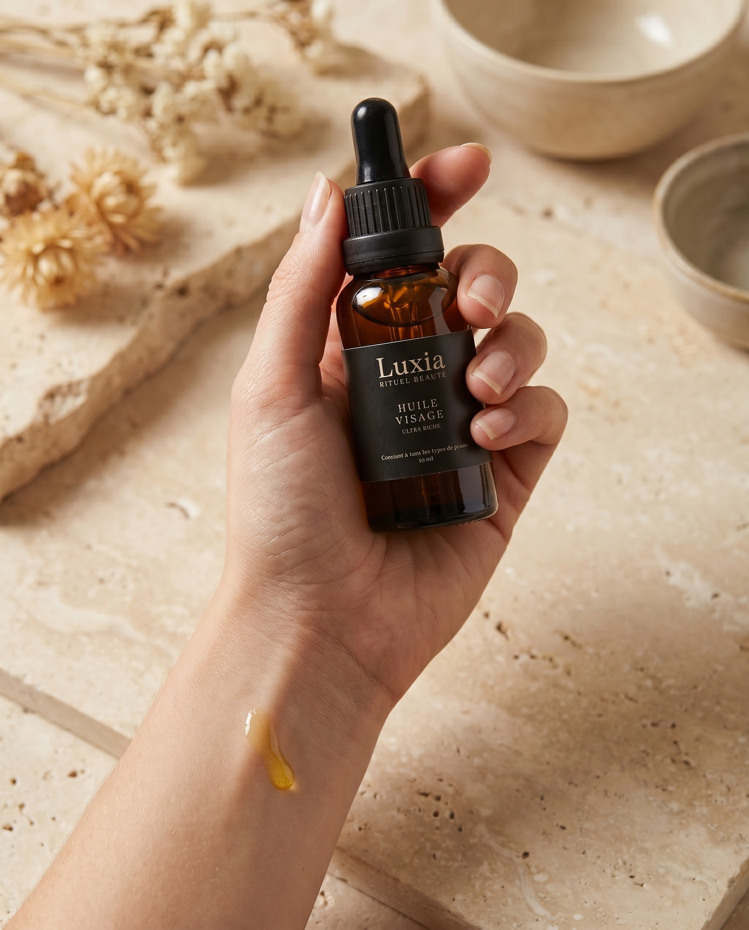 Main tenant l'Huile Visage Luxia avec une goutte d'huile — rituel sensoriel